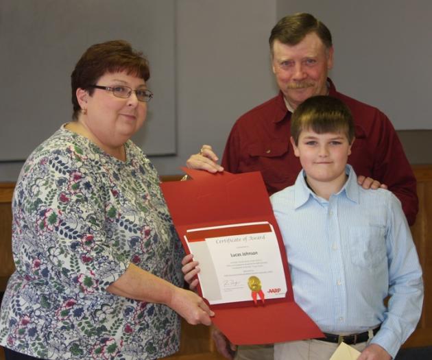 Phyllis Tate presents Lucas Johnson with a certificate for his winning essay as Pap Leroy Johnson looks on.