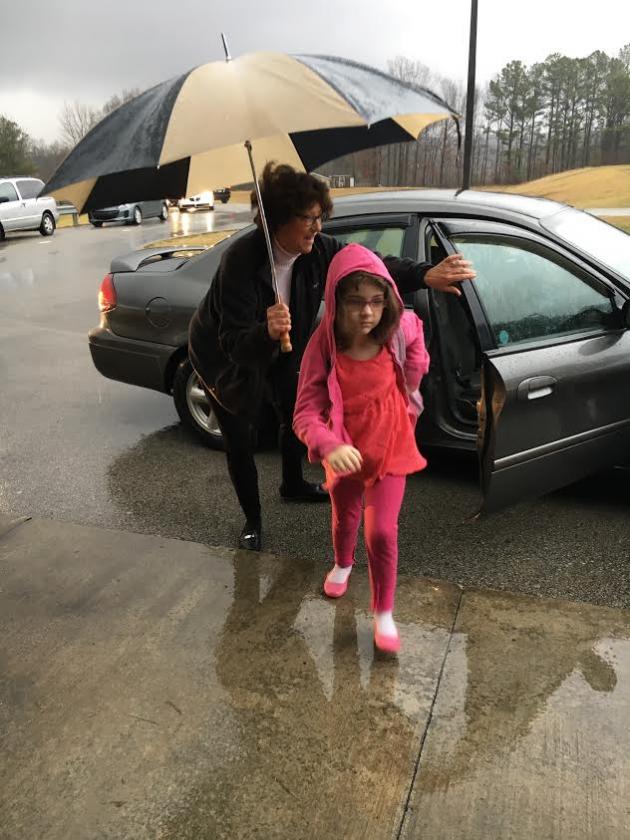 MES Counselor JoLynn Reed helps Cheyenne Givens, a kindergarten students in Mrs. Stokes class try to stay dry on a rainy day.