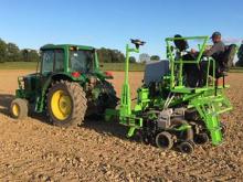 Technicians plant 4 row plots for the Kentucky Corn Variety Trial.  The technician riding the planter is changing corn hybrids on the go by dumping a small amount of seeds as the planter moves down the field.  The tractor is operating on auto-steer to insure even spacing between planter passes.